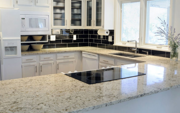 white granite countertops adorn this modern kitchen and highlight the black backsplash and white trimmings.