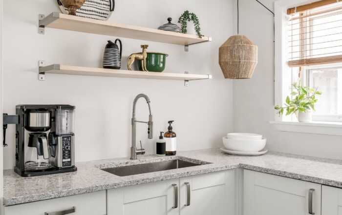 Modern kitchen with open shelving above a granite countertop, featuring stylish decor items, a coffee maker, and natural light from a nearby window.