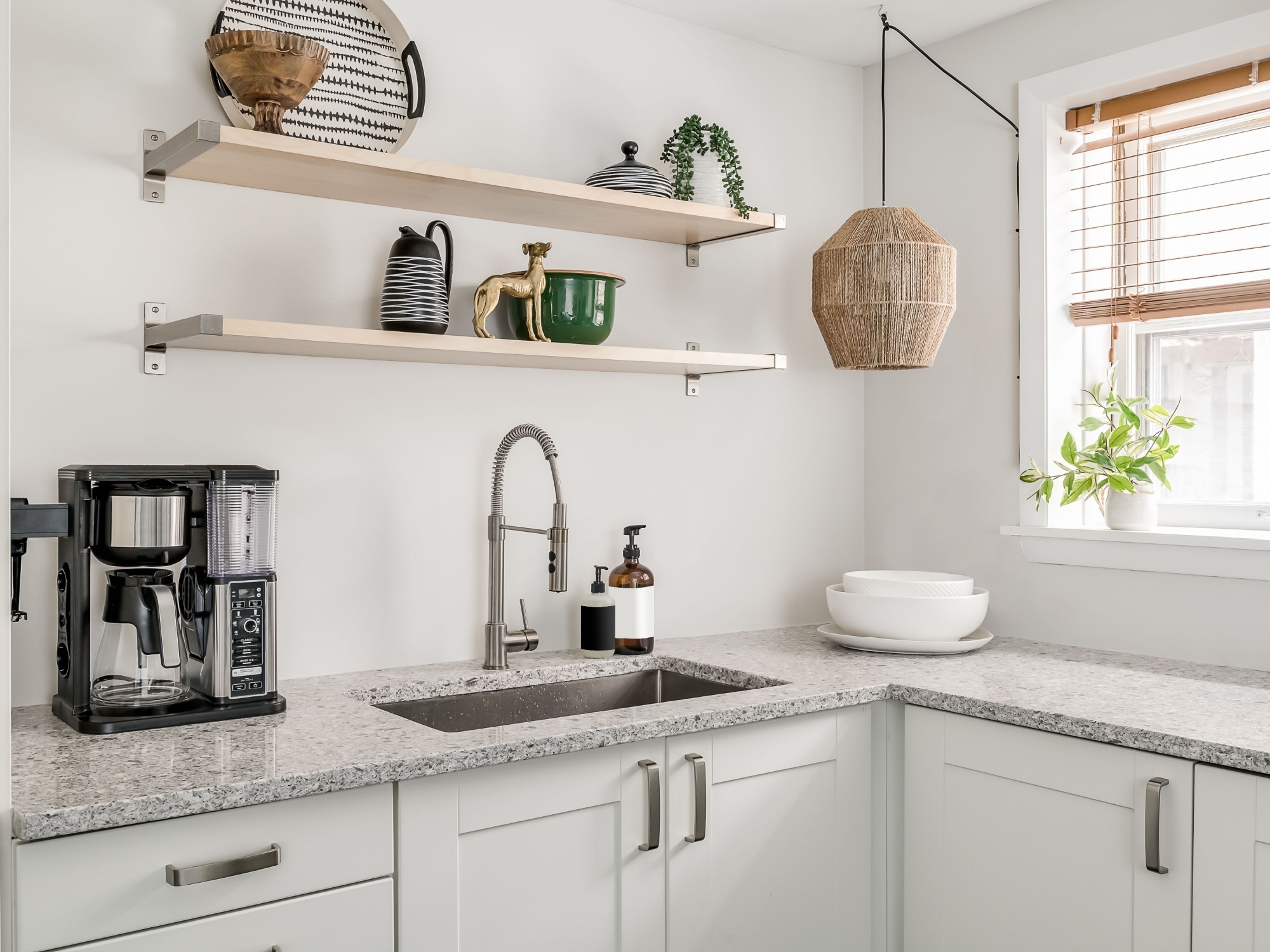 Modern kitchen with open shelving above a granite countertop, featuring stylish decor items, a coffee maker, and natural light from a nearby window.